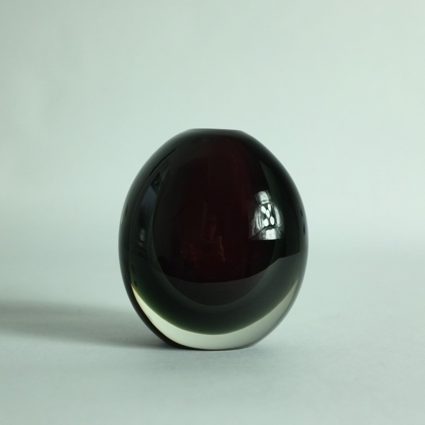 A small, heavy, round glass vase with deep red and grey submerged colors overlaid in clear.