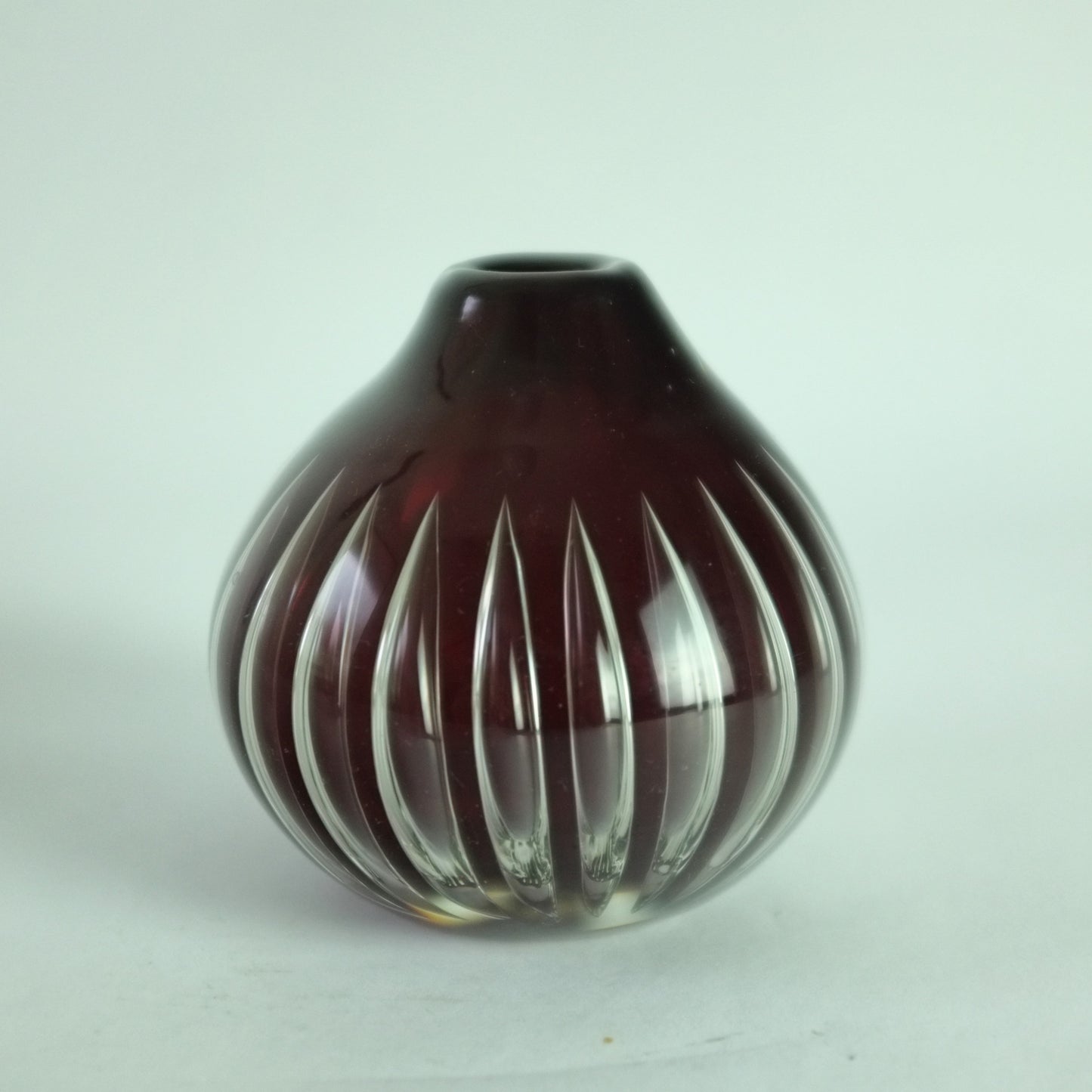 A deep red, onion-shaped glass vase with vertical trapped air decoration designed by Kaj Franck.