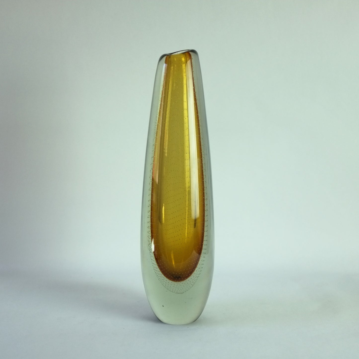 A tall free-blown glass vase with trapped air bubbles, featuring a yellow core and clear glass casing.