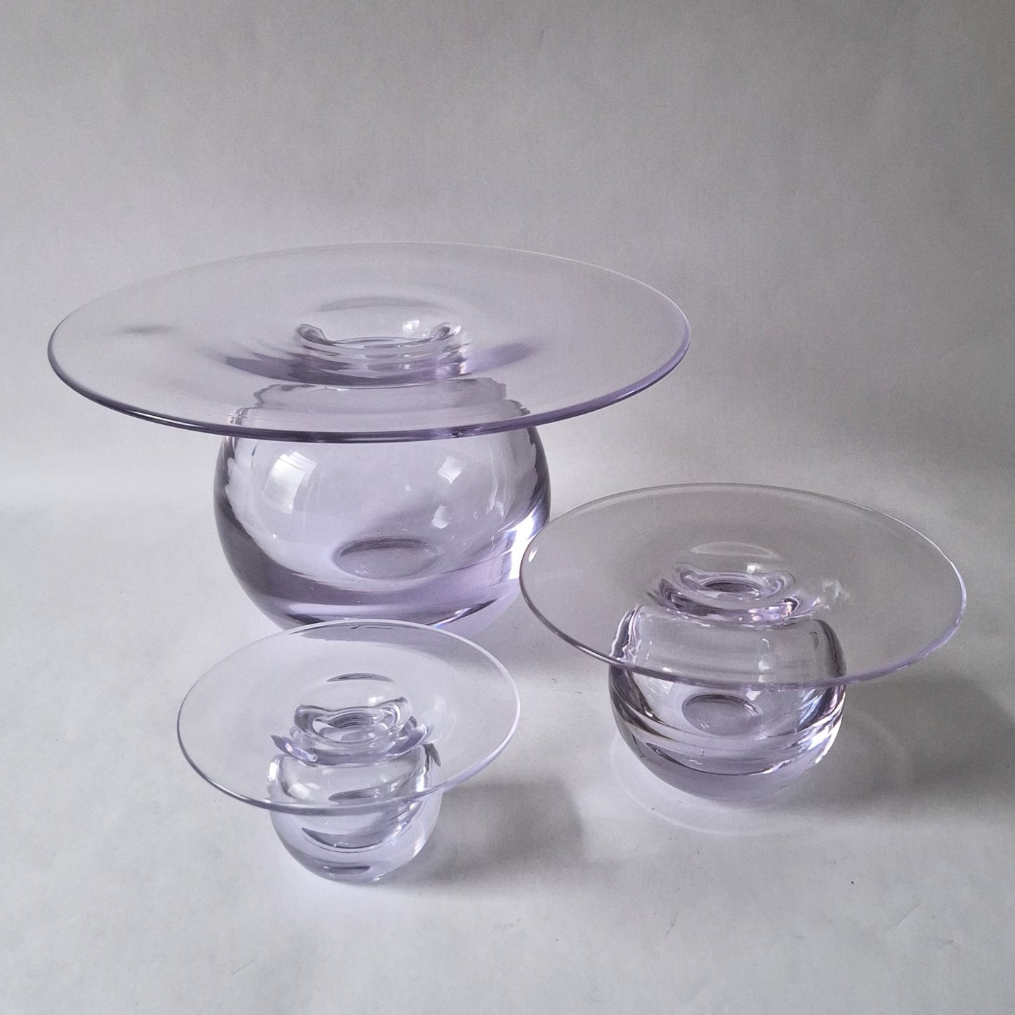 A set of three graduated clear glass vases with a wide flat rim above a spherical body, designed by Nanny Still.
