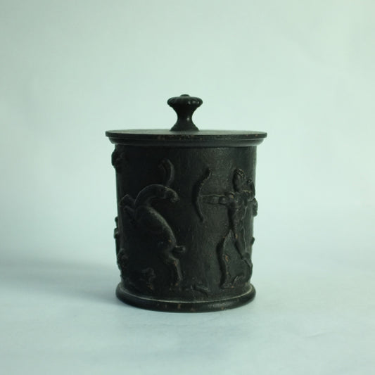 A black cast iron lidded pot with relief decoration of hunting scene.