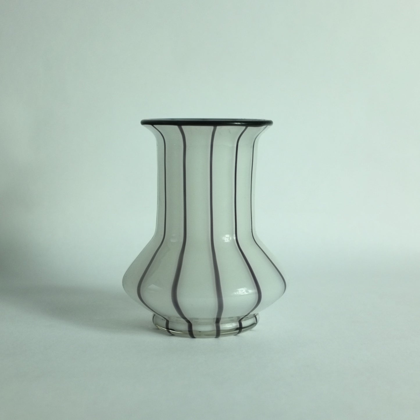 A white glass vase with black applied stripes and a black rim.