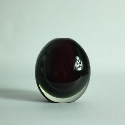A small, heavy, round glass vase with deep red and grey submerged colors overlaid in clear.