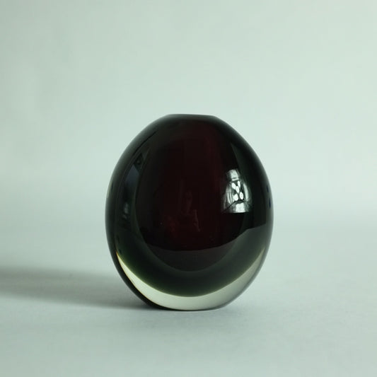 A small, heavy, round glass vase with deep red and grey submerged colors overlaid in clear.
