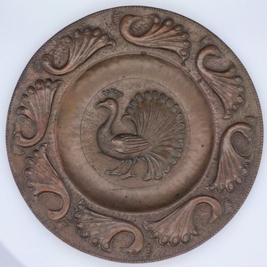 A copper charger with a central motif of a standing peacock, surrounded by eight stylized peacock designs around the edge.
