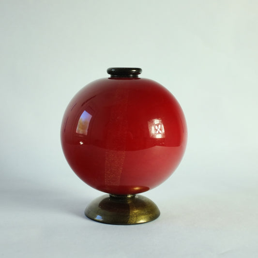 A spherical lattimo cased vase in deep red on domed black foot and applied black rim, all overlaid with gold leaf.