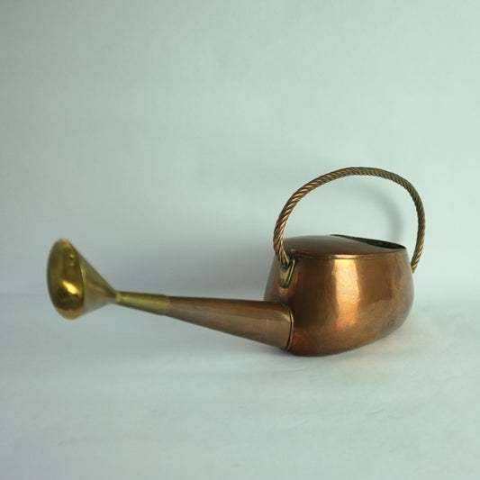 A vintage copper and brass watering can with a twisted copper wire handle and brass rose.
