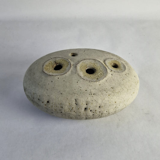 A low oval stoneware pebble with four potholes, featuring a creamy white glaze over a textured surface.