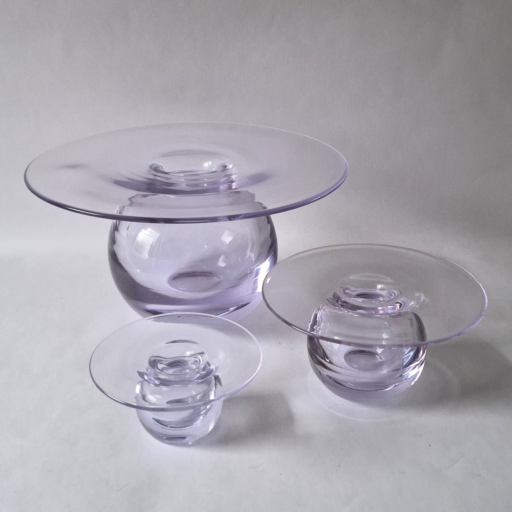 A set of three graduated clear glass vases with a wide flat rim above a spherical body, designed by Nanny Still.